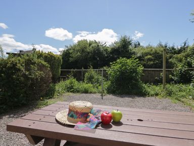 A wooden picnic table with a straw hat and two apples in a garden at 12 Eamont Park in Penrith