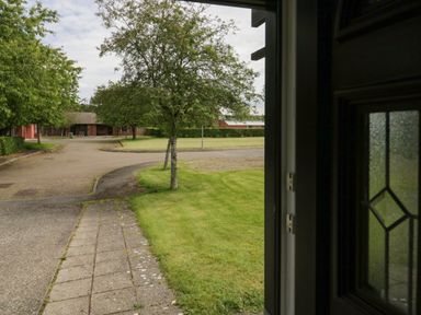 A view of a sidewalk and grassy area with trees and buildings in the background at 9 Eamont Park in Penrith