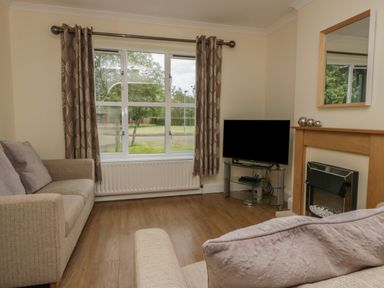 A living room with two sofas a television on a glass stand a fireplace and a large window at 9 Eamont Park in Penrith