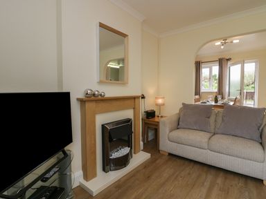 A living room with a sofa and cushions a fireplace a television and a dining area visible through an archway at 9 Eamont Park in Penrith