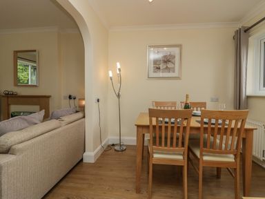 A dining area with a wooden table and four chairs next to a window and a living room with a beige sofa and a floor lamp at 9 Eamont Park in Penrith