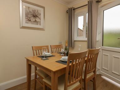 A dining area with a wooden table set with plates glasses and a bottle near a window and door at 9 Eamont Park in Penrith