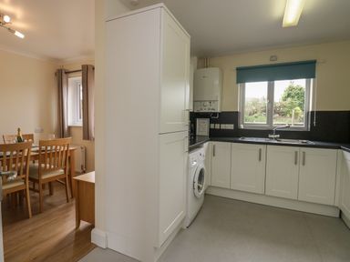 A kitchen with white cabinets washing machine and a dining area with a wooden table and chairs at 9 Eamont Park Penrith
