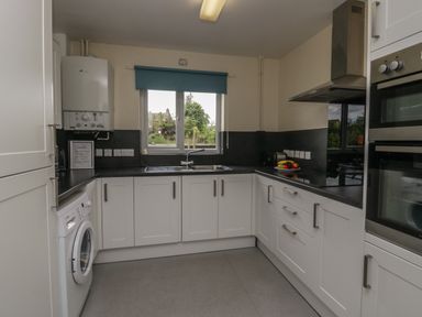 A kitchen with white cabinets a washing machine a double oven a stove with an extractor fan and a window with a blue blind at 9 Eamont Park in Penrith