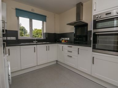 A kitchen with white cabinets a black countertop a window with a blue blind and built in ovens at 9 Eamont Park in Penrith