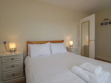 A bedroom with a bed with white sheets and pillows bedside tables with lamps a door with a mirror and a decorative wall hanging at 9 Eamont Park in Penrith