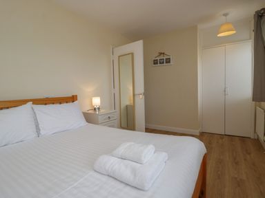 A bedroom with a wooden bed and white linens towels on the bed a white nightstand with a lamp a door with a mirror and a white closet at 9 Eamont Park in Penrith