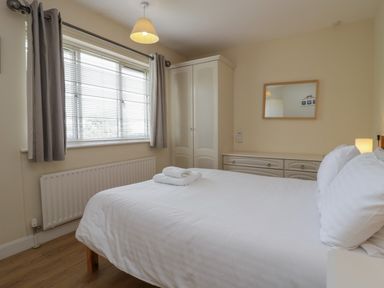 A bedroom with a bed and white linens a window with blinds and curtains a wardrobe a dresser with a mirror at 9 Eamont Park Penrith