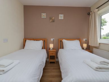 A bedroom with two single beds wooden headboards bedside table with lamps and butterfly wall art at 9 Eamont Park in Penrith