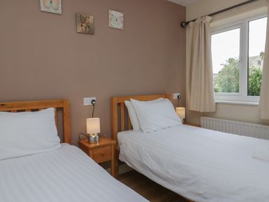 A bedroom with two single beds bedside tables lamps and a window with curtains at 9 Eamont Park in Penrith