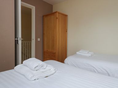 A bedroom with two single beds and a wooden wardrobe at 9 Eamont Park in Penrith