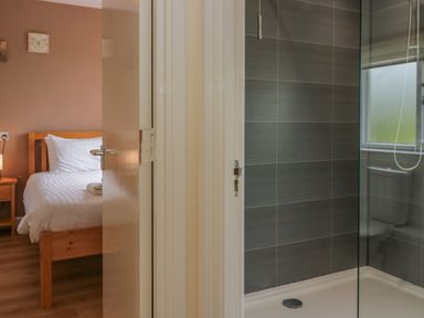 A bedroom with a bed and bedside table next to a bathroom with a shower at 9 Eamont Park Penrith