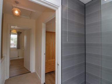 A hallway with doors leading to rooms and a corner of a tiled shower at 9 Eamont Park in Penrith