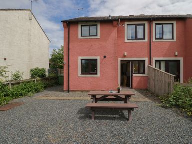 A backyard with a wooden picnic table and a pink house with brown framed windows and doors at 9 Eamont Park in Penrith