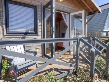 A small patio with a gray wooden chair and yellow cup outside a wooden house with open glass doors at Sea Spray in Lyme Regis