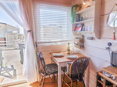 A small dining table with two chairs and a bottle of wine near a window with blinds and shelves at Sea Spray in Lyme Regis
