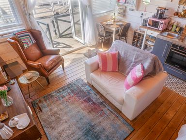 A living area with a white sofa with pink pillows a brown armchair a colorful rug a wooden floor and a small dining table near a kitchen at Sea Spray Lyme Regis