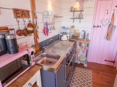 A small kitchen with a pink microwave copper pots hanging and a pink door at Sea Spray in Lyme Regis