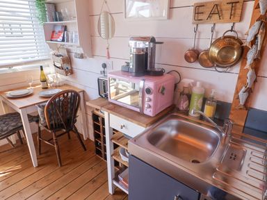 A small kitchen with a wooden table set for two a pink microwave coffee machine and stainless steel sink at Sea Spray Lyme Regis