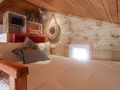 A bedroom with a wooden bed frame and pillows under a slanted wooden ceiling at Sea Spray in Lyme Regis
