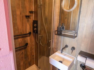 A small bathroom with a shower area wooden walls a white sink with black faucet and a mirror shelf at Sea Spray in Lyme Regis