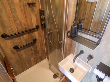A small bathroom with a shower enclosure a white sink black fixtures and wood paneled walls at Sea Spray in Lyme Regis