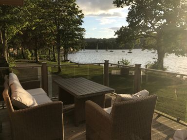 An outdoor seating area with a table and cushioned chairs overlooking a lake with boats and trees at Loubi's Lakeside Lodge M1 Fallbarrow Park near Bowness-On-Windermere