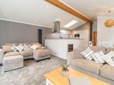 A living room with sofas and cushions next to an open kitchen with a skylight at Loubi's Lakeside Lodge M1 Fallbarrow Park near Bowness-On-Windermere