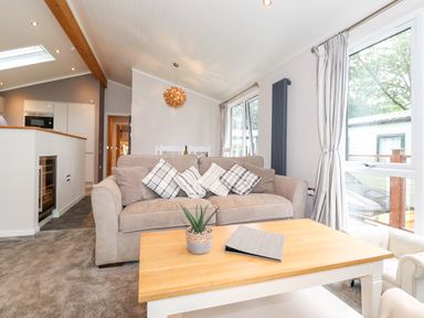 A living room with a beige sofa cushions a wooden coffee table and large windows at Loubi's Lakeside Lodge M1 Fallbarrow Park near Bowness-On-Windermere