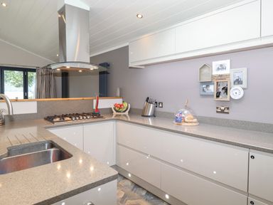 A kitchen with a sink a gas stove a fruit bowl knife set and a food cover on the counter at Loubi's Lakeside Lodge M1 Fallbarrow Park near Bowness-On-Windermere