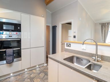 A kitchen with built in oven microwave white cabinets a sink and countertop at Loubi's Lakeside Lodge M1 Fallbarrow Park near Bowness-On-Windermere