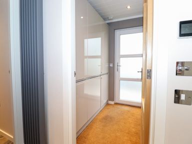 A hallway with white cabinets on the left and a frosted glass door at Loubi's Lakeside Lodge M1 Fallbarrow Park near Bowness-On-Windermere