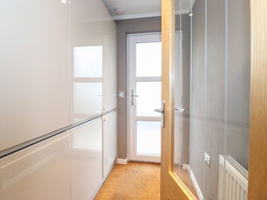 A hallway with glossy white cabinets carpeted floor and a glass door leading outside at Loubi's Lakeside Lodge M1 Fallbarrow Park near Bowness-On-Windermere