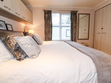 A bedroom with a bed pillows window with curtains built in wardrobes and a mirror at Loubi's Lakeside Lodge M1 Fallbarrow Park near Bowness-On-Windermere