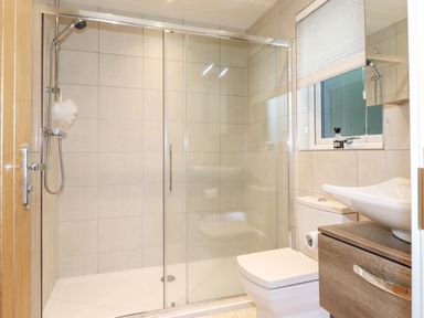 A bathroom with a glass shower enclosure a wall-mounted showerhead a toilet and a sink on a wooden vanity at Loubi's Lakeside Lodge M1 Fallbarrow Park near Bowness-On-Windermere