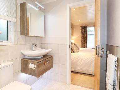 A bathroom with a sink cabinet toilet and a door leading to a bedroom at Loubi's Lakeside Lodge M1 Fallbarrow Park near Bowness-On-Windermere