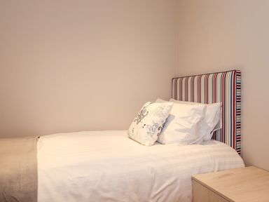 A bedroom with a single bed striped headboard and pillows beside a wooden nightstand at Loubi's Lakeside Lodge M1 Fallbarrow Park near Bowness-On-Windermere