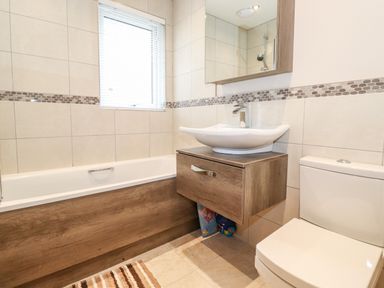 A bathroom with a bathtub a sink with cabinet a toilet and a window at Loubi's Lakeside Lodge M1 Fallbarrow Park near Bowness-On-Windermere