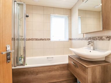 A bathroom with a bathtub a shower a sink with a cabinet and a window at Loubi's Lakeside Lodge M1 Fallbarrow Park near Bowness-On-Windermere