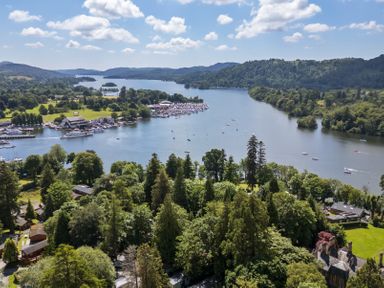 A lake surrounded by trees hills and buildings with boats on the water at Loubi's Lakeside Lodge M1 Fallbarrow Park near Bowness-On-Windermere