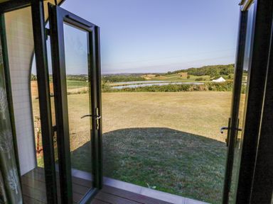 An open glass door leading to a grassy lawn with a pond and hills in the background at Ailsa Craig in Hillhampton Great Witley