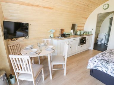 A small kitchen and dining area with a round table set for four and a television on the wall at Ailsa Craig in Hillhampton Great Witley