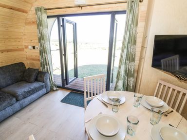 A dining area with plates and glasses on a round table next to a sofa and glass doors with curtains at Ailsa Craig in Hillhampton Great Witley