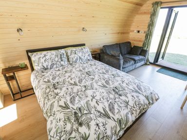 A bedroom with a bed covered in floral bedding a gray sofa and sliding glass doors at Ailsa Craig in Hillhampton Great Witley