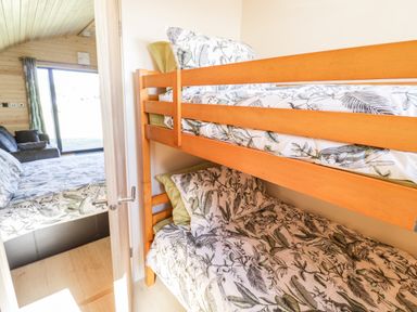 A room with wooden bunk beds and floral bedding next to a bedroom with a bed and a sofa at Ailsa Craig in Hillhampton Great Witley