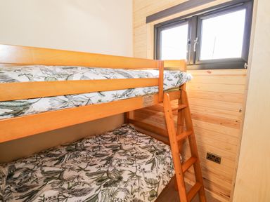 A bunk bed with floral bedding next to a window in a wooden paneled room at Ailsa Craig in Hillhampton Great Witley