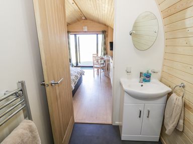 A bathroom with a sink, round mirror and towel rack looking into a bedroom with a bed, dining table and open doors at Ailsa Craig in Hillhampton Great Witley