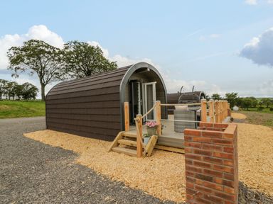 An outdoor wooden pod with a small porch and seating area surrounded by wood chips at Laird Lodge 2 in Lochmaben