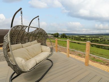 A woven hanging outdoor chair on a wooden deck overlooking green fields and hills at Laird Lodge 2 in Lochmaben