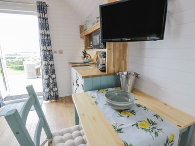 A small kitchen area with a wooden table and chairs a television mounted on the wall and a sliding door leading outside at Laird Lodge 2 Lochmaben